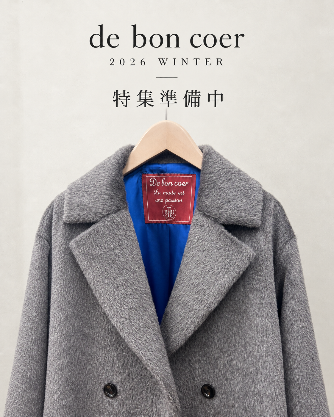 de bon coer 2026 WINTER 特集準備中。青い裏地と赤いブランドタグが見えるグレーのコート。