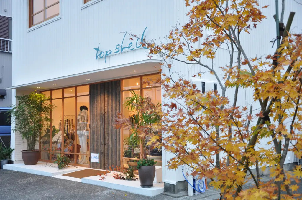 トップシェルの店舗外観。白い建物に青い看板、入口と秋色の木。
